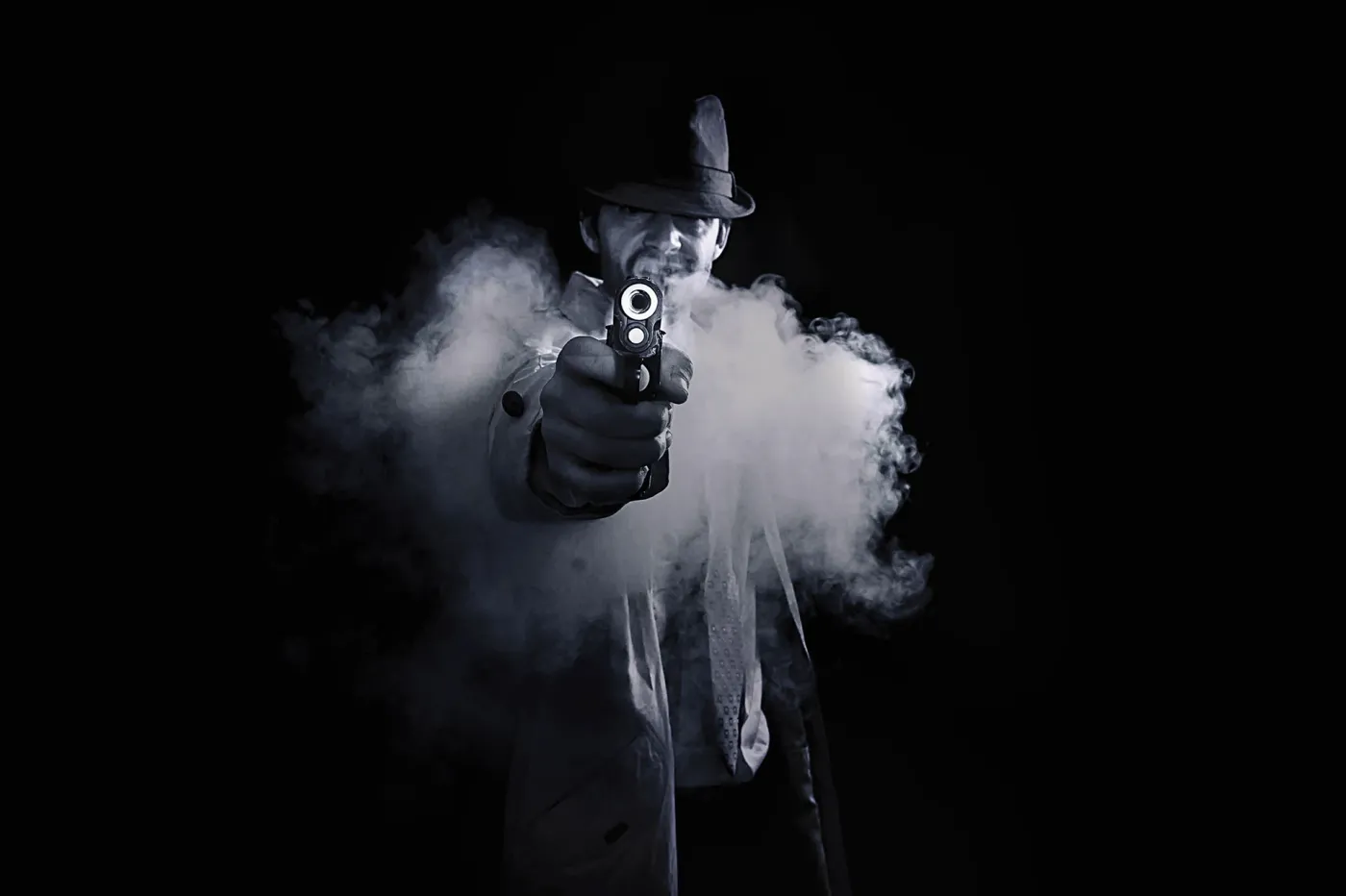 Caracterización de Ademar Silvoso como detective clásico con chapeu fedora, gabardina e pistola entre fume